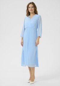 Svijetloplava midi haljina s naborima, dizajnom omote, dugim rukavima i glatkom teksturom, uparen a sa kremasto bijelim potpeticama.