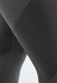 Detailní záběr na tmavě šedou texturovanou látku s viditelným šitím na oděvu, která zdůrazňuje vlastnosti materiálu a detaily švů.