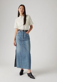 Šviesios spalvos trumpas rankovėmis marškinėliai, aukšto liemens džinsinė maksi sijonas su šoniniu plyšiu ir juodos blokinės kulno platforminės šlepetės. Paprastas dizainas, kasdieniškas stilius.