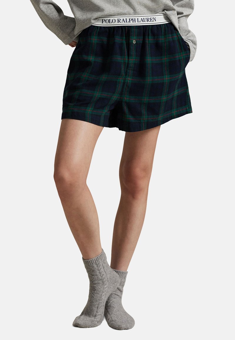 Rutiga bomullsshorts med marinblå bas och gröna och röda linjer, med en elastisk midja som har varumärkesdetaljer. I kombination med grå stickade strumpor.