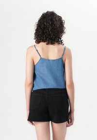 Canottiera di denim con spalline sottili, caratterizzata da un davanti blu chiaro e un retro blu scuro, abbinata a pantaloni corti neri a vita alta.