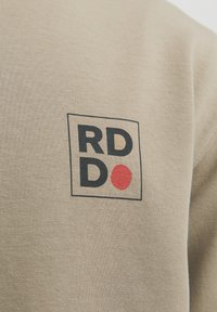 Beige cotton fabric with a subtle texture. Features a logo with "RD" in black, "DO" in dark blue, and a red dot inside a square frame.