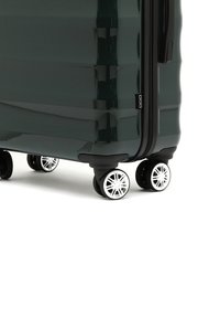 Valigia rigida di colore verde scuro con finitura lucida, dotata di quattro ruote multidirezionali e chiusura a zip.