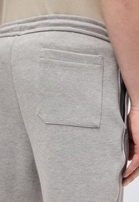 Κοντινό πλάνο στο ισχίο ενός ατόμου που φοράει ανοιχτό γκρι υφασμάτινο παντελόνι με τετράγωνη πίσω τσέπη και μπεζ πουκάμισο που έχει μπει μέσα στο παντελόνι.