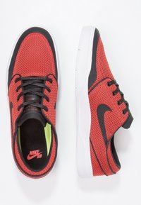 Baskets rouges texturées avec des accents noirs, dotées d'une semelle blanche, de lacets noirs et d'une semelle intérieure verte. Logo Nike SB visible sur la languette.