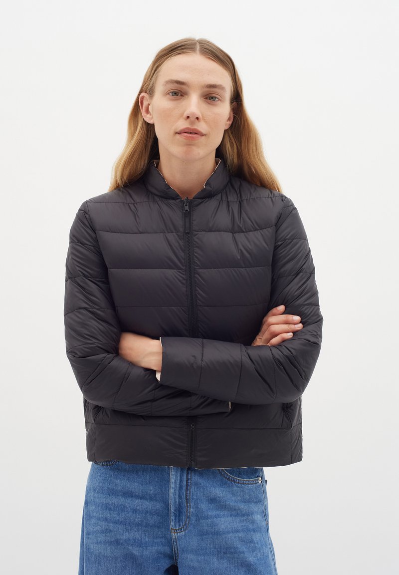 Schwarze gepolsterte Bomberjacke mit hohem Kragen und Frontreißverschluss. Verfügt über horizontale Nähte und ein kurzes Design. Kombiniert mit blauen Jeans.