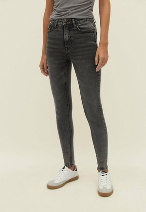 Jeans skinny negros con una cintura alta, que cuentan con cinco bolsillos y un ligero desvanecido. Combinados con zapatillas blancas y una camiseta gris ajustada.