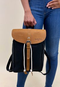 Czarny plecak z płótnem o połysku z klapą z brązowej skóry, regulowanymi paskami, zapięciem na sznurek i subtelnym logo wytłoczonym z przodu.