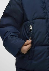 Granatowa kurtka puchowa o błyszczącej, gładkiej fakturze. Posiada zamykaną na zamek kieszeń boczną oraz grubą, puszystą konstrukcję z dopasowanym mankietem.