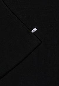 Tissu noir avec une petite étiquette blanche rectangulaire portant le mot "CECIL", cousue dans une couture au coin du tissu.
