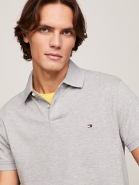 Grijze polo shirt met een kraag, twee knopen, korte mouwen en een klein logo met rode, witte en blauwe accenten.