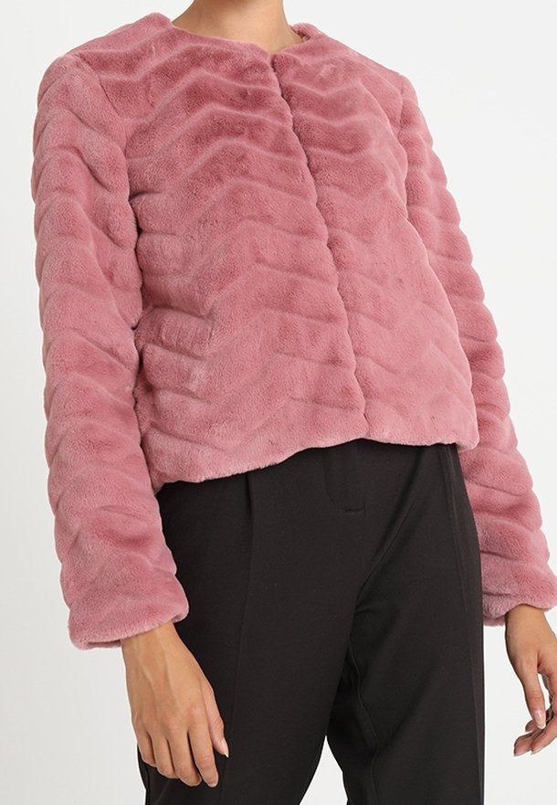 Veste moulante en fausse fourrure mauve avec une texture ondulée horizontale portée avec un pantalon noir, vue du cou jusqu’aux hanches.