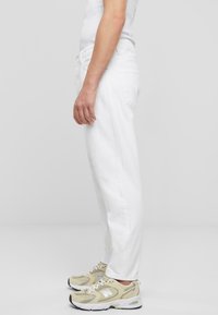 Pantalones de mezclilla blancos con detalles desgastados, corte recto y bolsillos laterales, combinados con zapatillas beiges con acentos grises y suelas blancas.