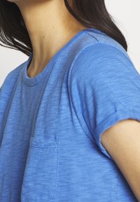 Blåmelerad kortärmad skjorta med rund halsringning och en bröstficka, med en mjuk textur och uppvikt ärmdetaljer.