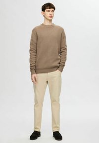 Maglione beige a maglia con collo rotondo, abbinato a pantaloni beige chiaro e scarpe scure. Il tessuto presenta un motivo testurizzato e polsini a costine.