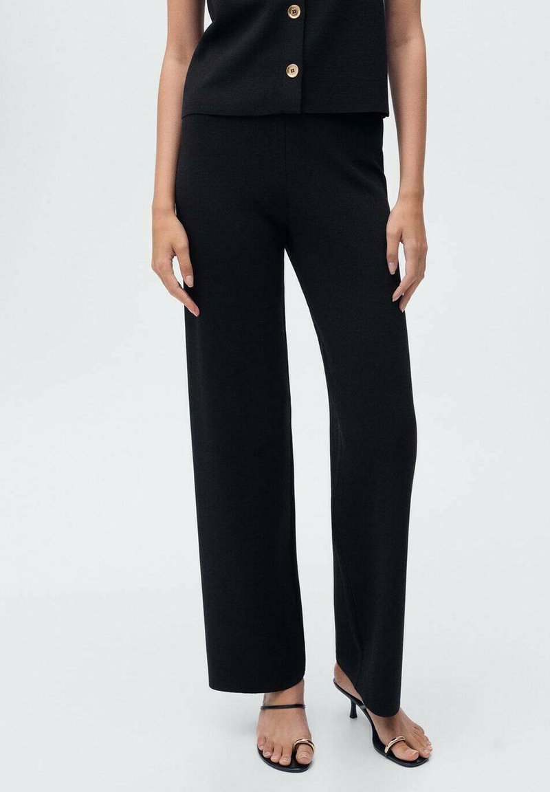 Pantalons larges noirs en tissu texturé, avec une taille mi-haute. Assortis avec des talons ouverts et un haut ajusté à boutons.