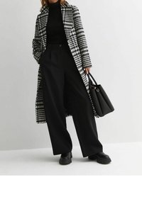 Abrigo largo de pata de gallo en blanco y negro sobre un suéter negro de canalé, combinado con pantalones amplios negros y un bolso estructurado negro.