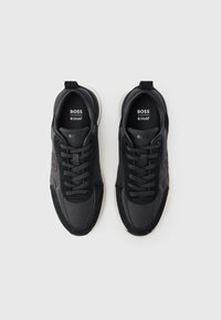 Mustat tennarit, jotka on valmistettu nahka- ja tekstiilimateriaalien sekoituksesta. Niissä on pyöreä kärki, teksturoidut pinnat ja pehmustettu pohja, jossa on nauhat.