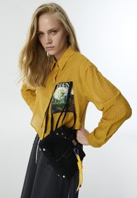 Borsa in suede nera con accenti gialli, forma rettangolare e lunghe tracolle. Presenta una maniglia gialla annodata e cuciture decorative.