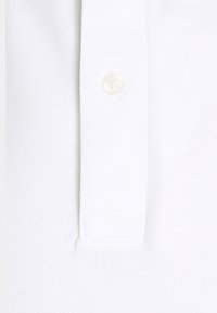 Gros plan d'une patte de chemise blanche avec un bouton blanc fermé au centre.