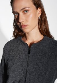 Giacca grigia con zip realizzata in tessuto testurizzato; presenta un colletto arrotondato e una zip frontale con un pull tab nero.