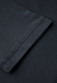 Tessuto blu scuro con una trama liscia, che presenta un polsino piegato e dettagli di cucitura visibili, catturato in primo piano.