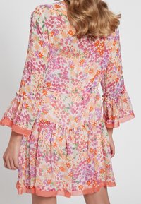 Květinové šaty z lehkého materiálu s vzory v růžové, oranžové a zelené barvě. Rukávy a lem zdobené volány s kontrastním broskvovým lemem.