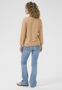 Lichtbruin, gebreid sweater met lange mouwen en een relaxte pasvorm, gecombineerd met lichtblauwe flared jeans met stikdetails op de achterzakken.
