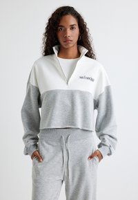 Geknipte pullover in grijs en wit, gemaakt van zacht materiaal. Heeft een hoge kraag met een halve rits en borduursel met de tekst "San Francisco."