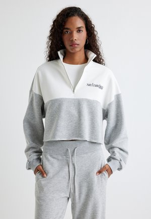 Gekürzter Pullover in Grau und Weiß, aus weichem Material. Verfügt über einen hohen Kragen mit einem Halbreißverschluss und einer Stickerei mit der Aufschrift "San Francisco."