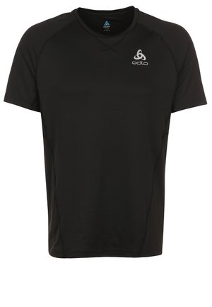 Mężczyzna w czarnej sportowej koszulce i szortach idący do przodu, ubrany w białe i niebieskie buty do biegania na jasnym, jednolitym tle.