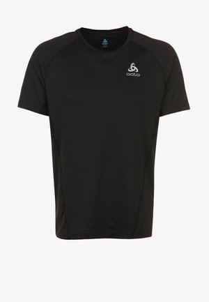Hombre con camiseta deportiva negra y pantalones cortos caminando hacia adelante, vistiendo zapatillas de correr blancas y azules sobre un fondo claro y liso.