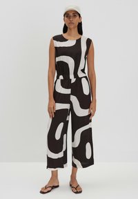 Zwart-wit jumpsuit met abstracte golvende patronen, zonder mouwen, elastische taille en wijde, verkorte benen. Gecombineerd met een lichte pet.