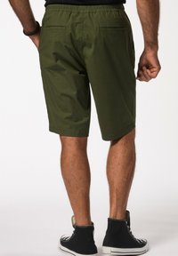 Grüne Shorts mit einem elastischen Bund und zwei Gesäßtaschen, aus leichtem Stoff gefertigt. Tragen mit schwarzen High-Top-Sneakern.