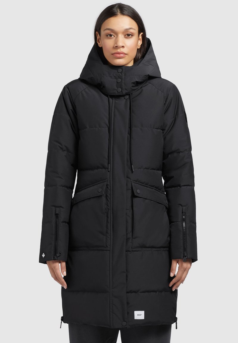 Black padded parka coat featuring a hood, zippered pockets, drawstrings, and a logo patch on the hem. Smooth texture, mid-length design.