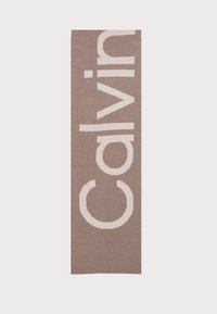 Tappeto con logo Calvin Klein, forma rettangolare, sfondo marrone chiaro, testo bianco in grassetto, texture morbida, design minimalista.