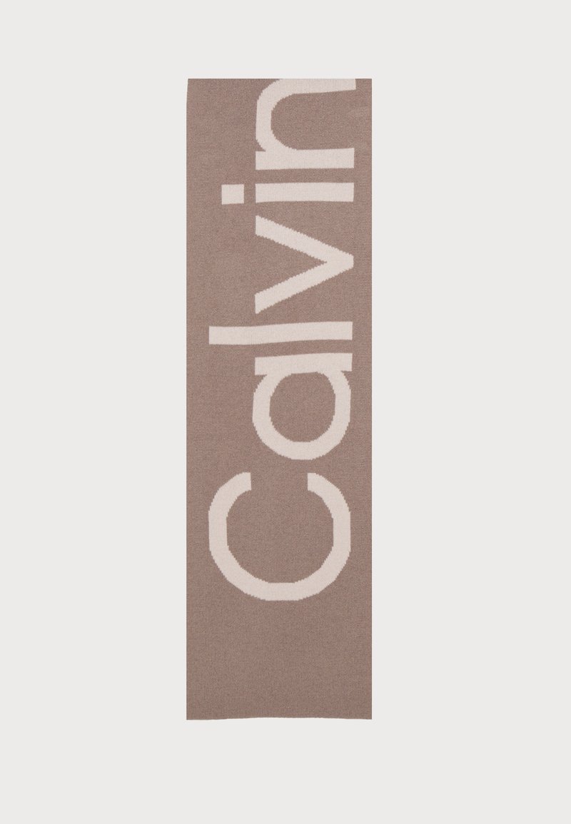 Tappeto con logo Calvin Klein, forma rettangolare, sfondo marrone chiaro, testo bianco in grassetto, texture morbida, design minimalista.