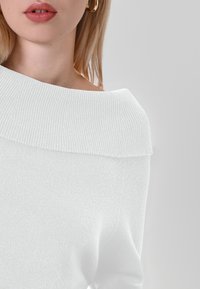 Maglione bianco ad off-shoulder con texture a coste e scollatura ampia. Materiale morbido con una leggera lucentezza.