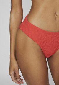 Bikini inferior texturizado rojo con un diseño de cintura alta, que presenta un patrón acanalado y bordes lisos para un ajuste ceñido.
