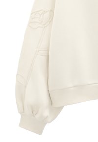Kremowa bluza z ribbowymi mankietami, z haftowanym wzorem róży na rękawie i teksturowanym materiałem.