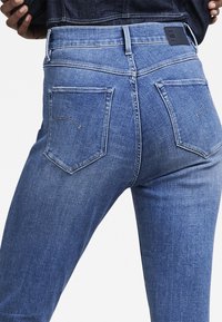 Jeans de mezclilla azul medio con una cintura alta, que cuentan con dos bolsillos traseros y costuras en contraste. Tienen un ajuste relajado y una textura suave.