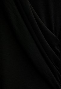 Tissu noir avec une texture froncée et des plis doux, créant un effet drapé. Le matériau est léger et lisse.