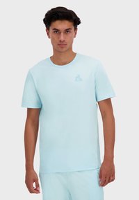 Světle modré bavlněné tričko s krátkými rukávy, kulatým výstřihem a malou grafikou na levé hrudi. Hladká textura a volný střih.