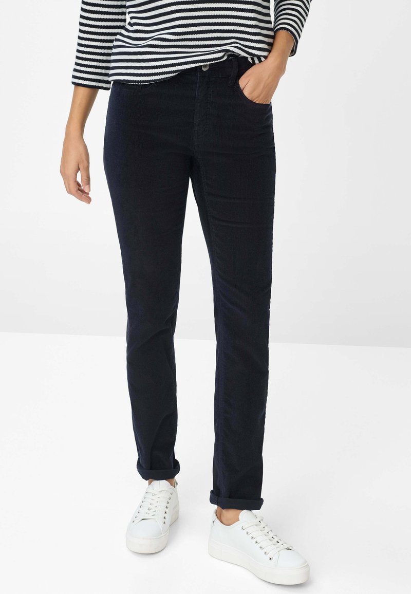Marineblauwe corduroy broek met een rechte pasvorm, voorzakken en opgerolde manchetten, gecombineerd met witte sneakers en een zwart-wit gestreepte top.