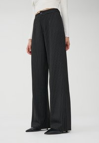 Pantaloni a gamba larga neri a righe con vita alta, chiusura frontale con bottone e una texture del tessuto liscia. Design sartoriale con silhouette allungata.
