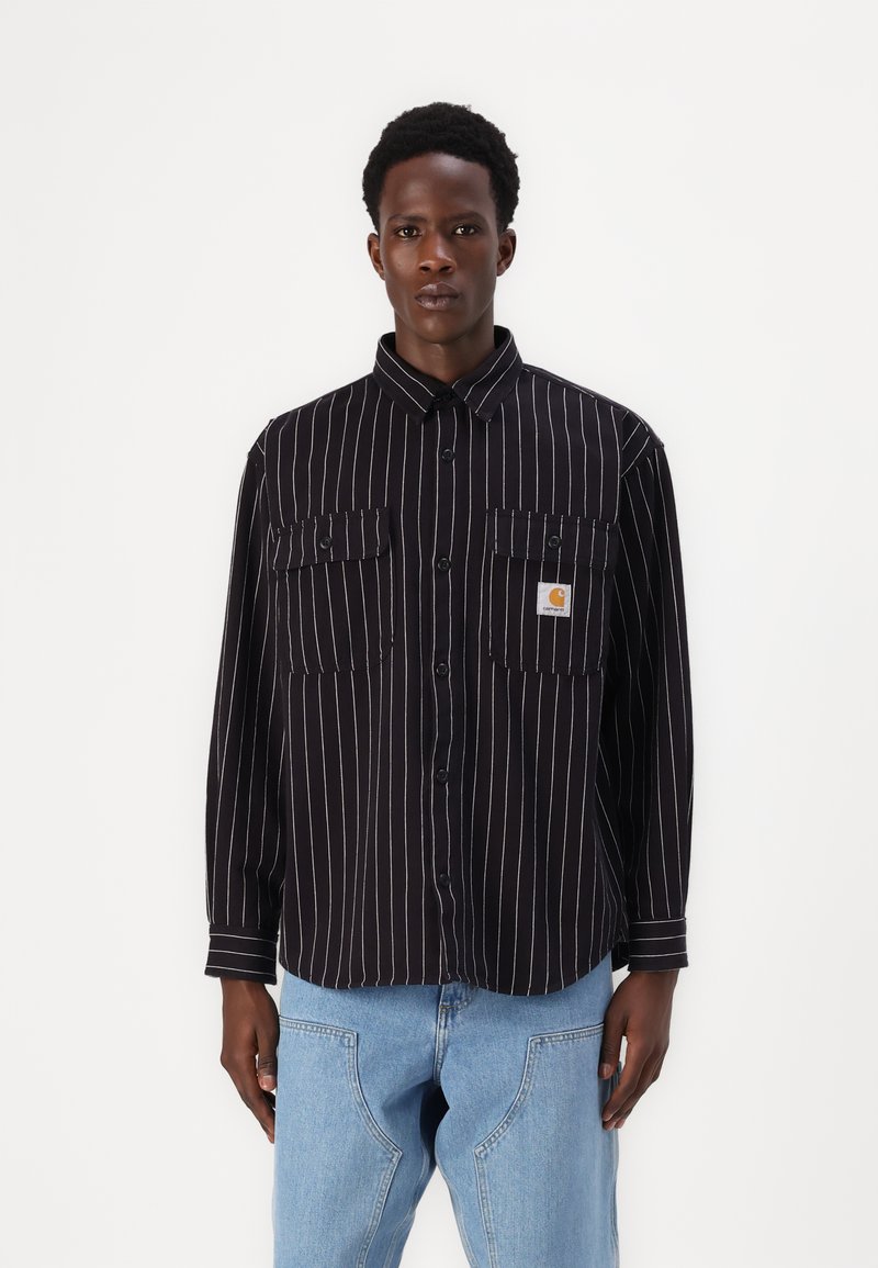 Black and white striped button-up shirt with two chest pockets, a collar, and a logo patch, featuring a relaxed fit and long sleeves.