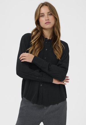 Zwarte_button-up_shirt_met_ronde_kraag_en_lange_mouwen,_gemaakt_van_gladde_stof._Voorzien_van_een_heél_bij_gebogen_zoom_en_subtiele_knopen_details.