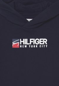 Felpa blu navy con tasca frontale, caratterizzata da un logo grafico bianco che include la scritta "Hilfiger" e "New York City" in grassetto.
