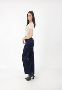 Beżowa dopasowana bluzka z krótkim rękawem w połączeniu z granatowymi spodniami o wysokim stanie oraz czarnymi botkami na obcasie. Gładki materiał z dopasowanym krojem i kieszeniami.