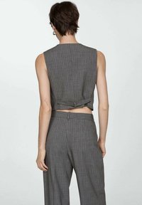 Chaleco a rayas grises con un diseño de espalda recortada, presenta una banda y un cierre de metal. Combina con unos pantalones a medida a juego.